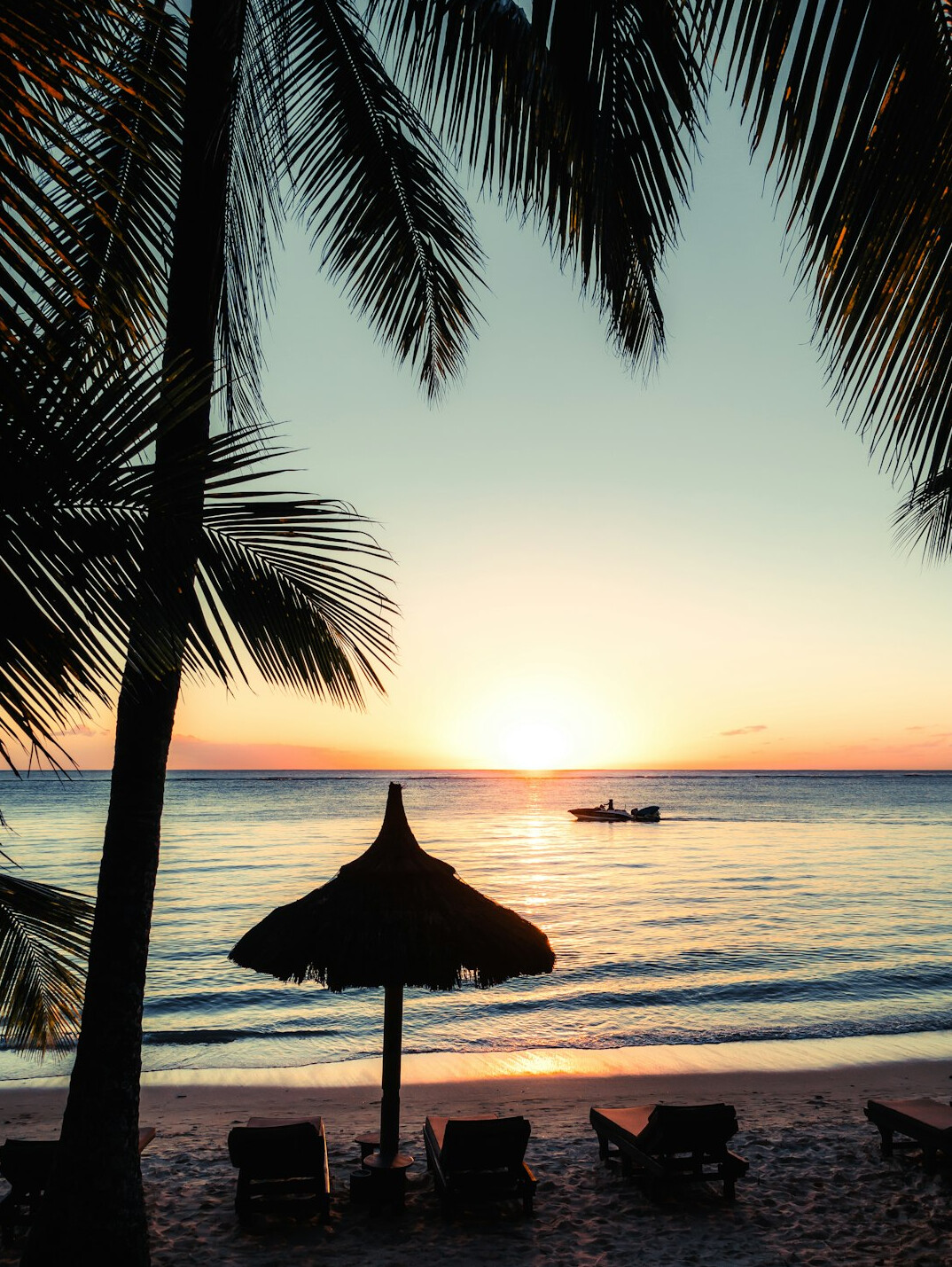 Tropical beach with turquoise water and sunbeds at sunset